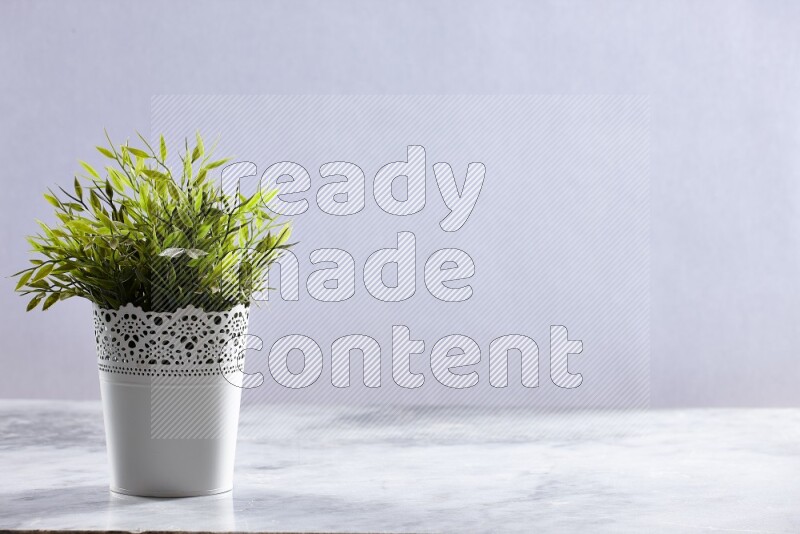 Green artificial plant in white decorative pot on grey marble background