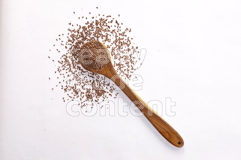 A wooden ladle full of flax seeds on a white flooring