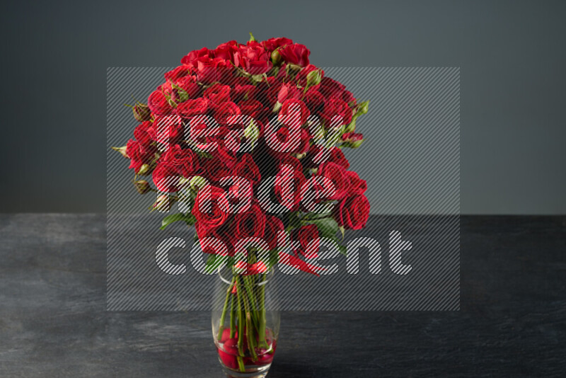 مجموعة من الورود الحمراء الزاهية المربوطة بإحكام بشريط أحمر في مزهرية زجاجية على خلفية من الرخام الأسود