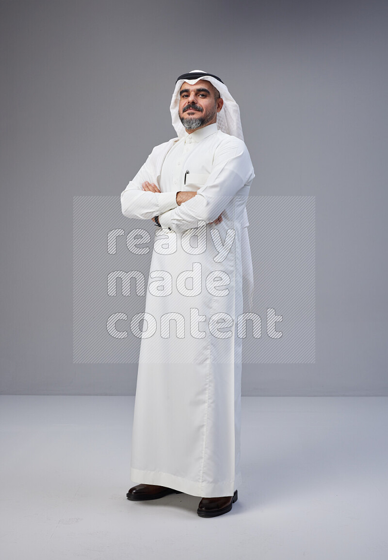 Saudi man Wearing Thob and white Shomag standing with crossed arms on Gray background