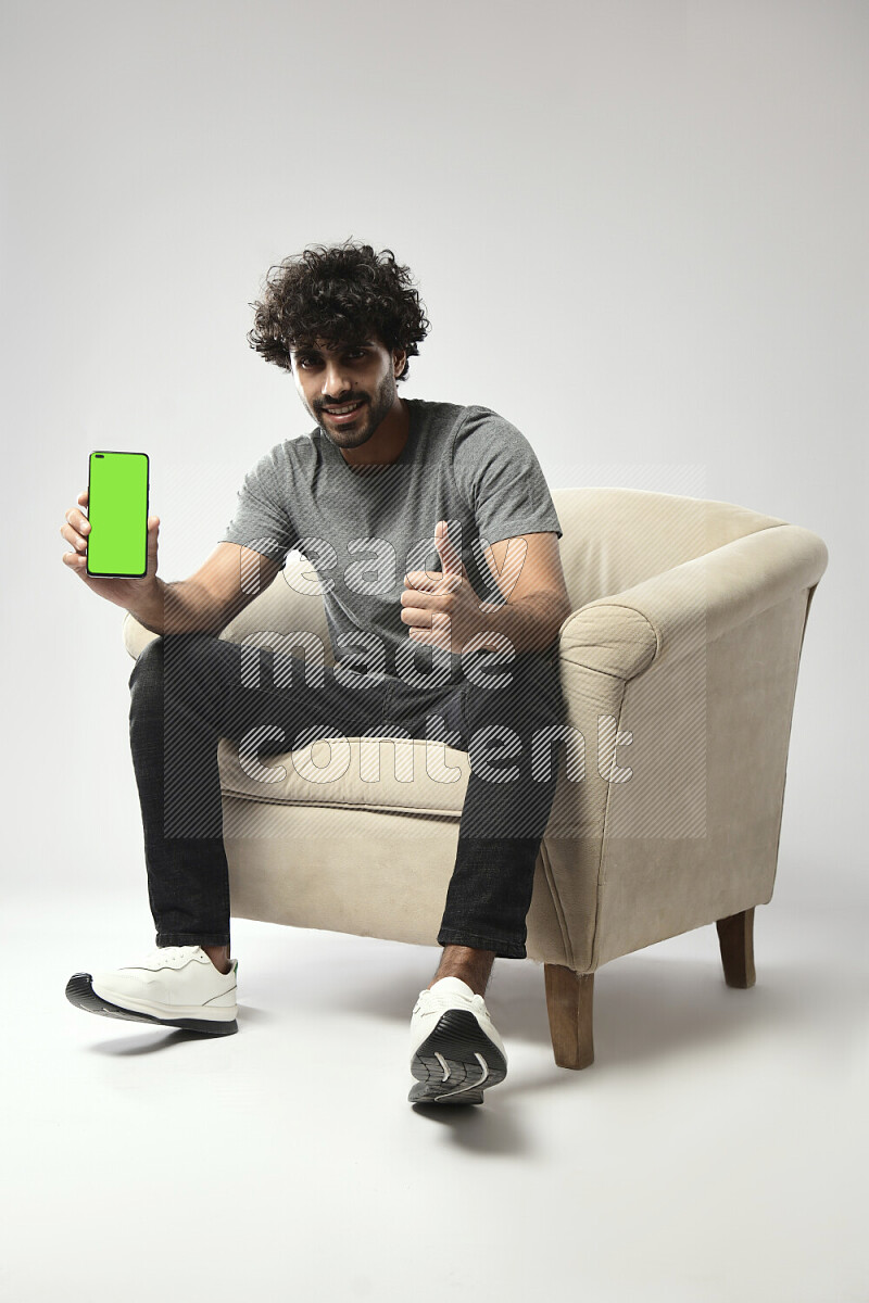 A man wearing casual sitting on a chair showing a phone screen on white background