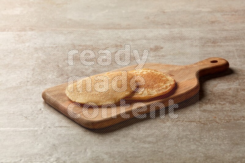 Two stacked plain pancakes on a wooden board on beige background