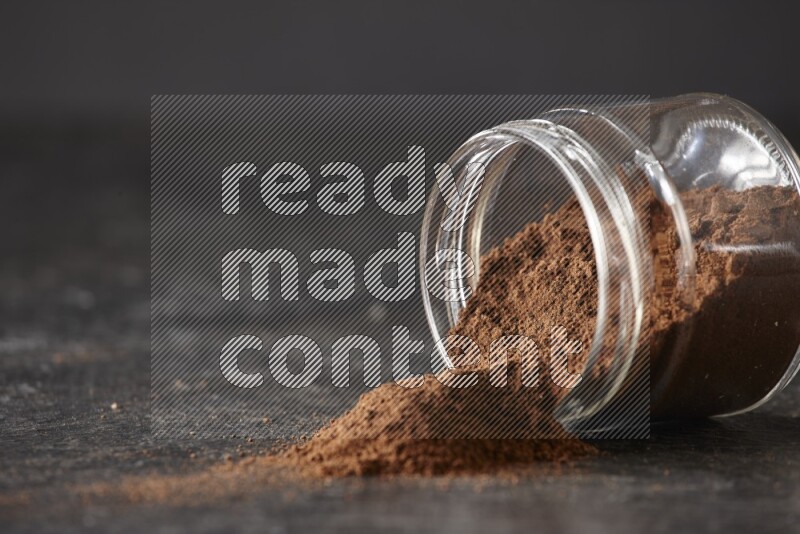 A flipped glass jar full of cloves powder on a textured black flooring