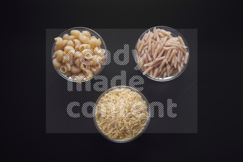 Different pasta types in glass bowls on black background