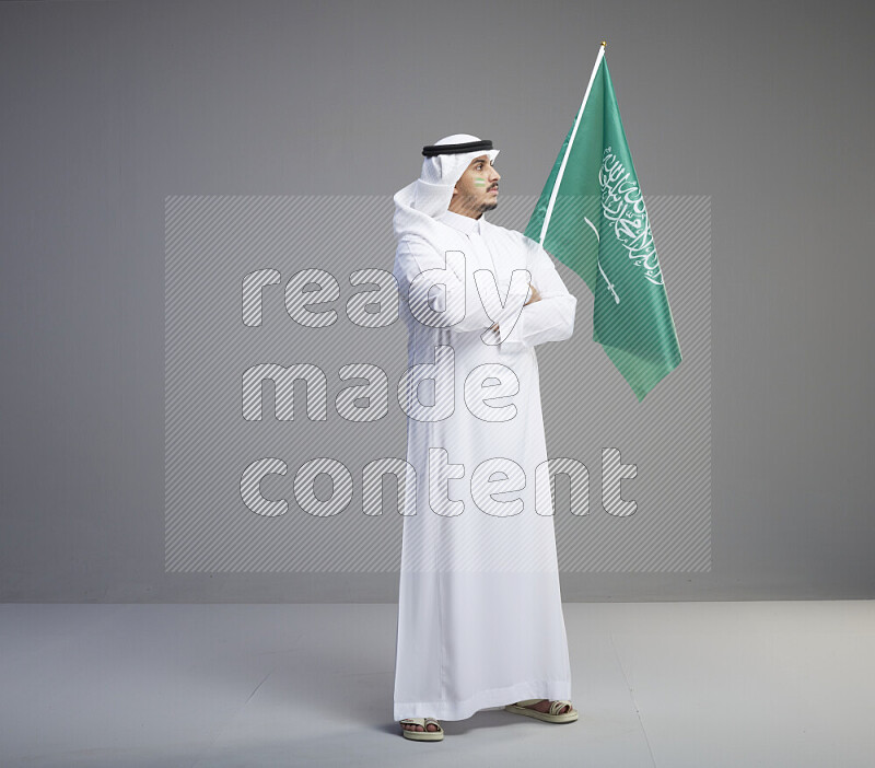 رجل سعودي يرتدي ثوب ابيض وشماغ ويحمل علم السعودية