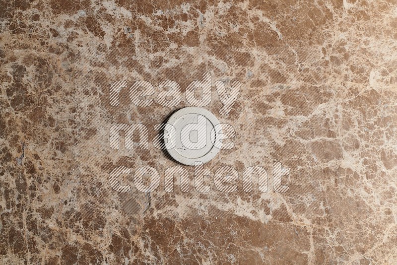 Top view shot of a pottery coaster tile on beige marble flooring