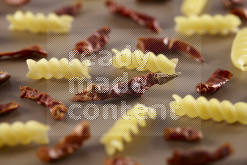 Raw pasta with different ingredients such as cherry tomatoes, garlic, onions, red chilis, black pepper, white pepper, bay laurel leaves, rosemary and cardamom on beige background
