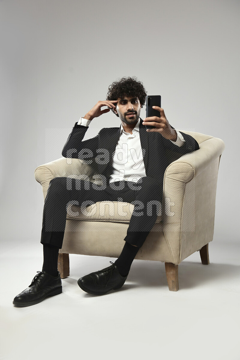 A man wearing formal sitting on a chair browsing on the phone on white background