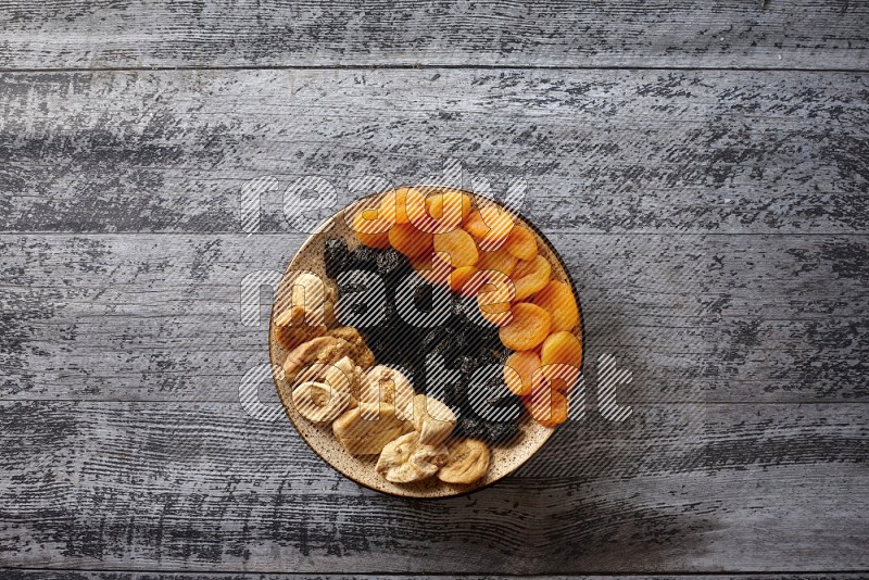 Dried fruits in a pottery plate with nuts and coffee in a dark setup