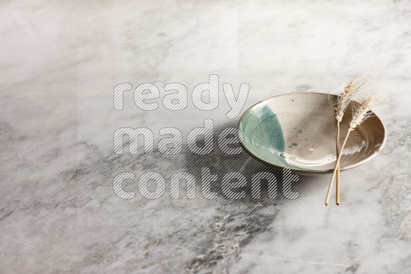Wheat stalks on multicolored pottery plate on grey marble background