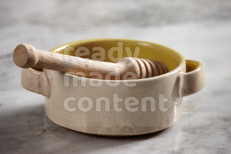 Multicolored pottery bowl with wooden honey dipper in it on grey marble background