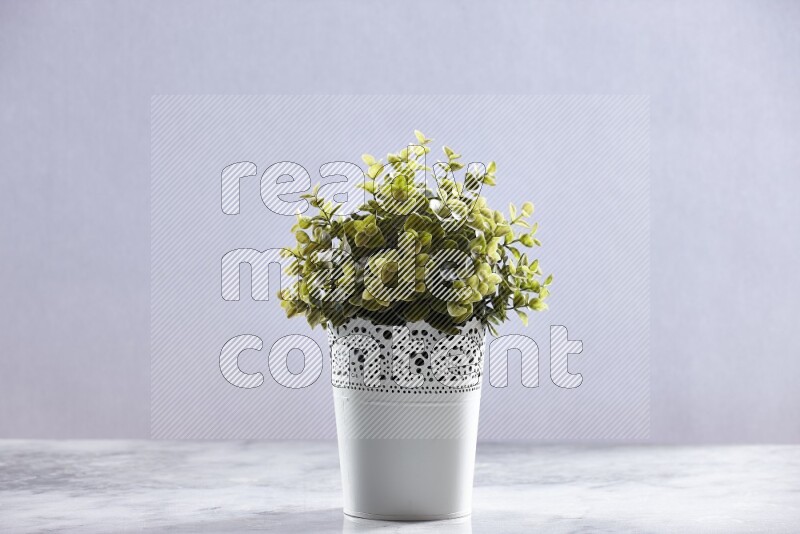 Green artificial plant in white decorative pot on grey marble background