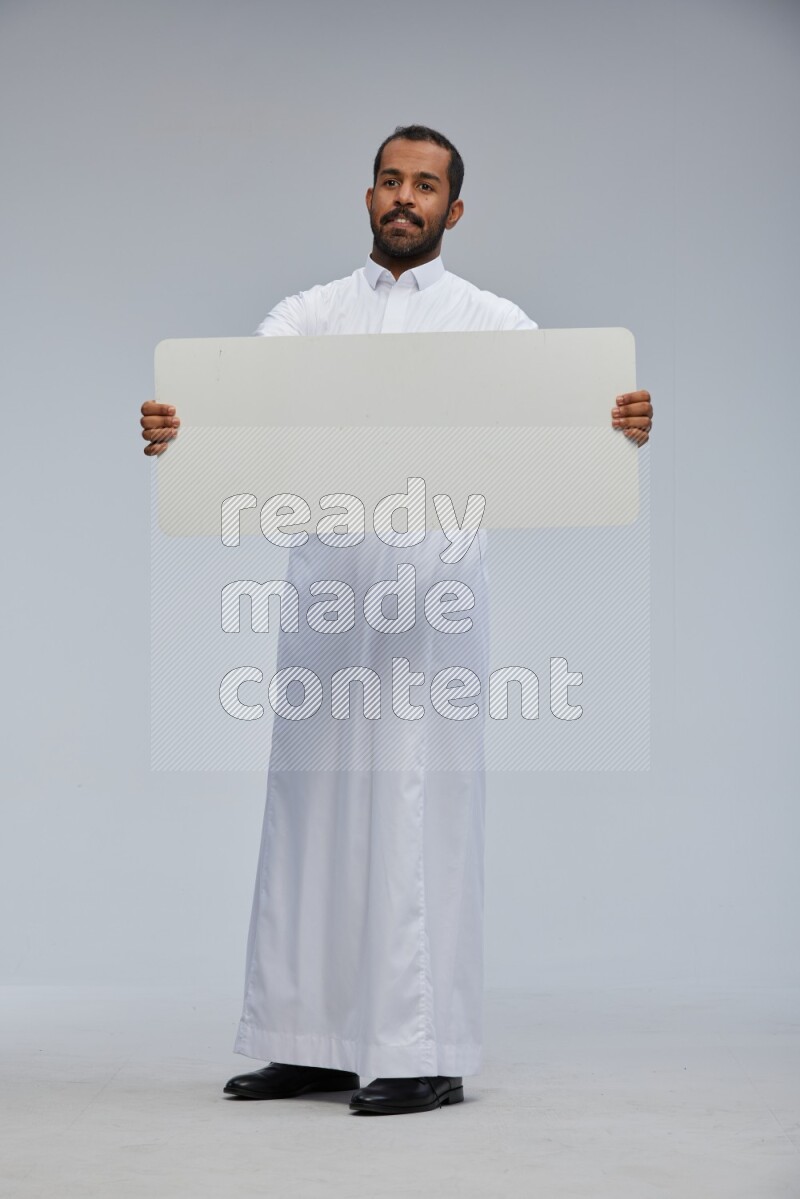 Saudi man wearing Thob standing holding board on Gray background