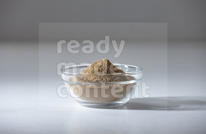 A glass bowl full of cumin powder on a white flooring