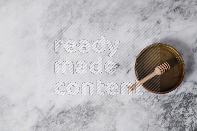 Multicolored pottery oven plate with wooden honey dipper in it on grey marble background