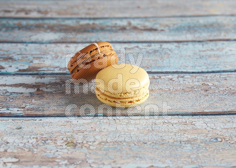 45º Shot of of two assorted Brown Irish Cream, and Yellow Vanilla macarons on light blue background