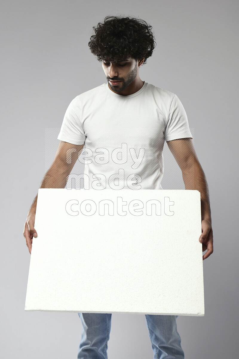 رجل يرتدي ملابس كاجوال يحمل لوحة بيضاء علي خلفية بيضاء