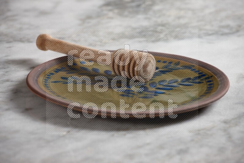 Decorative pottery plate with wooden honey dipper in it on grey marble background