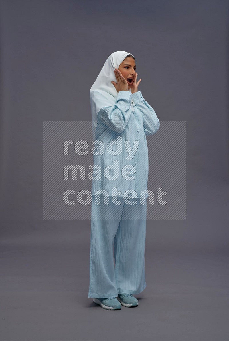 Saudi woman wearing hijab clothes standing interacting with the camera on gray background