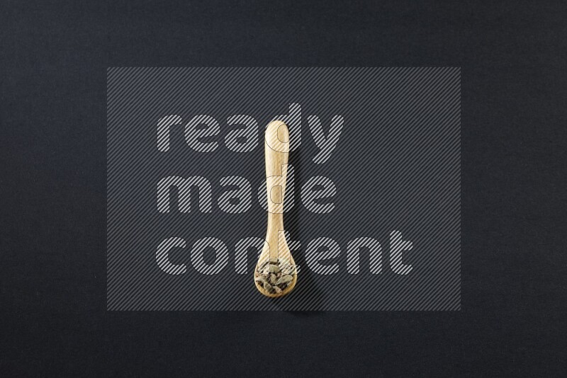 ملعقة خشبية ممتلئة بالهيل على خلفية سوداء