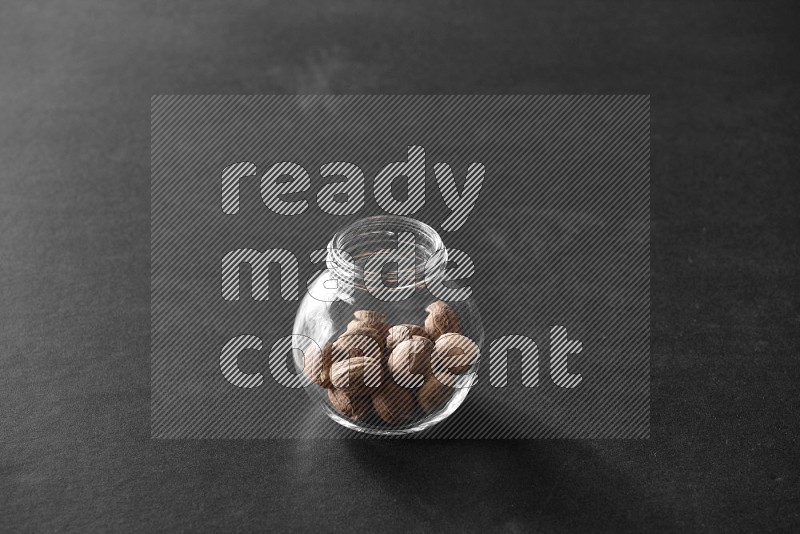 A glass spice jar full of nutmeg on black flooring