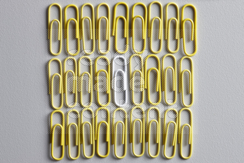 A bunch of yellow paper clips with a different colored paper clip in the center on grey background