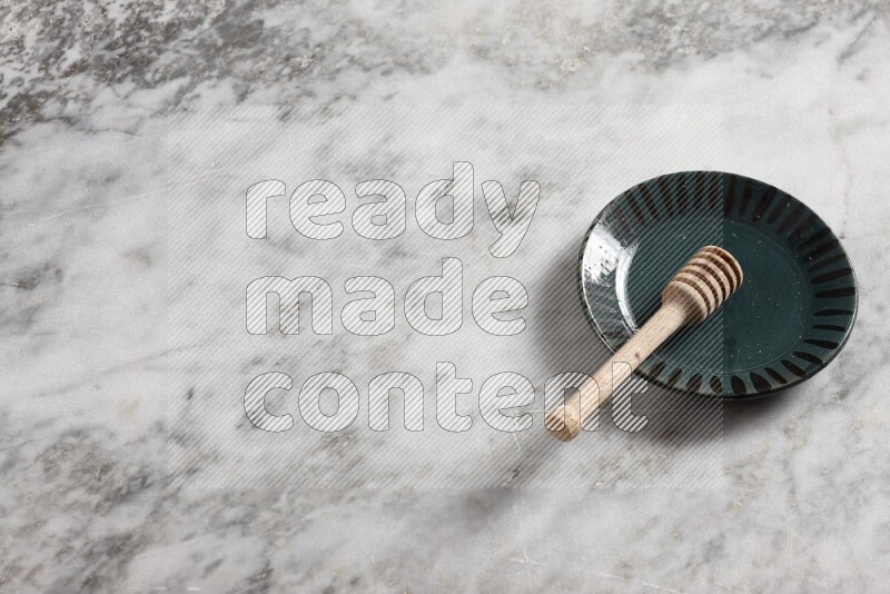 Multicolored pottery plate with wooden honey dipper in it on grey marble background