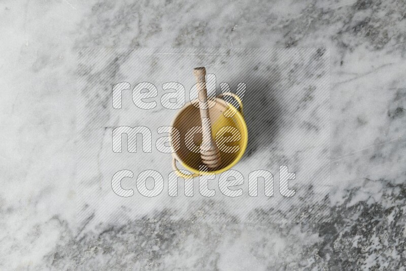 Multicolored pottery bowl with wooden honey dipper in it on grey marble background