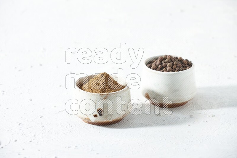 2 beige bowls, one full of allspice powder and the other full of whole balls on a textured white flooring