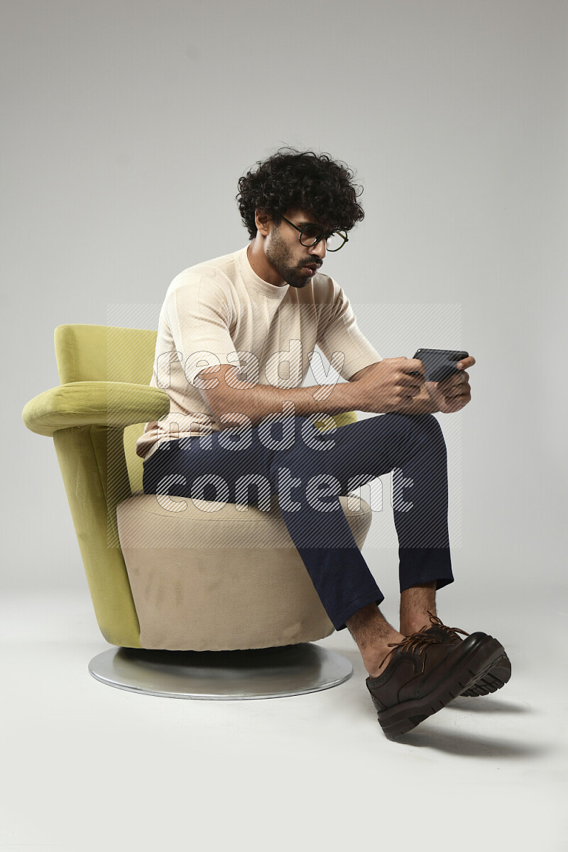 A man wearing casual sitting on a chair gaming on the phone on white background