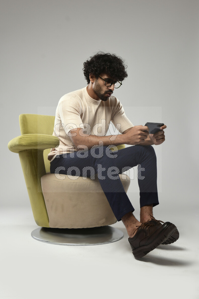 A man wearing casual sitting on a chair gaming on the phone on white background