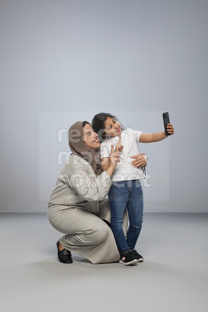 A girl standing taking selfie with her mother on gray background