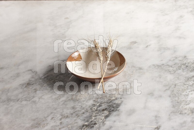 Wheat stalks on multicolored pottery plate on grey marble background