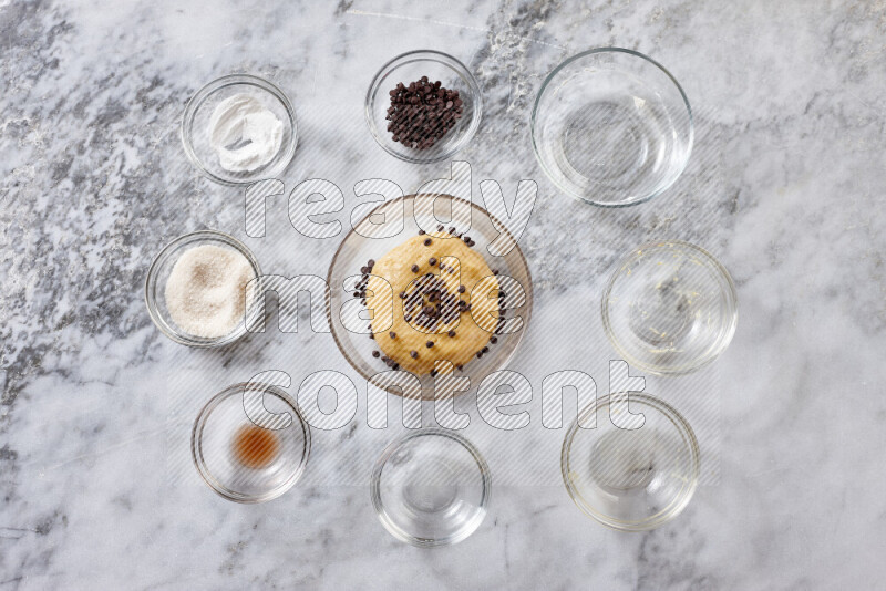 Cookies step by step with its ingredient, flour, butter, brown sugar, egg, vanilla extract, white sugar, chocolate chips and baking soda on grey marble background
