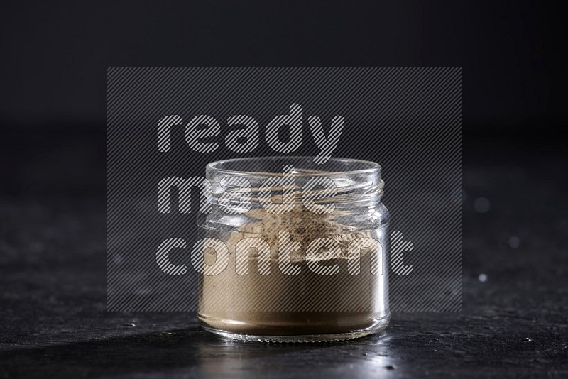 A glass jar full of garlic powder on a textured black flooring