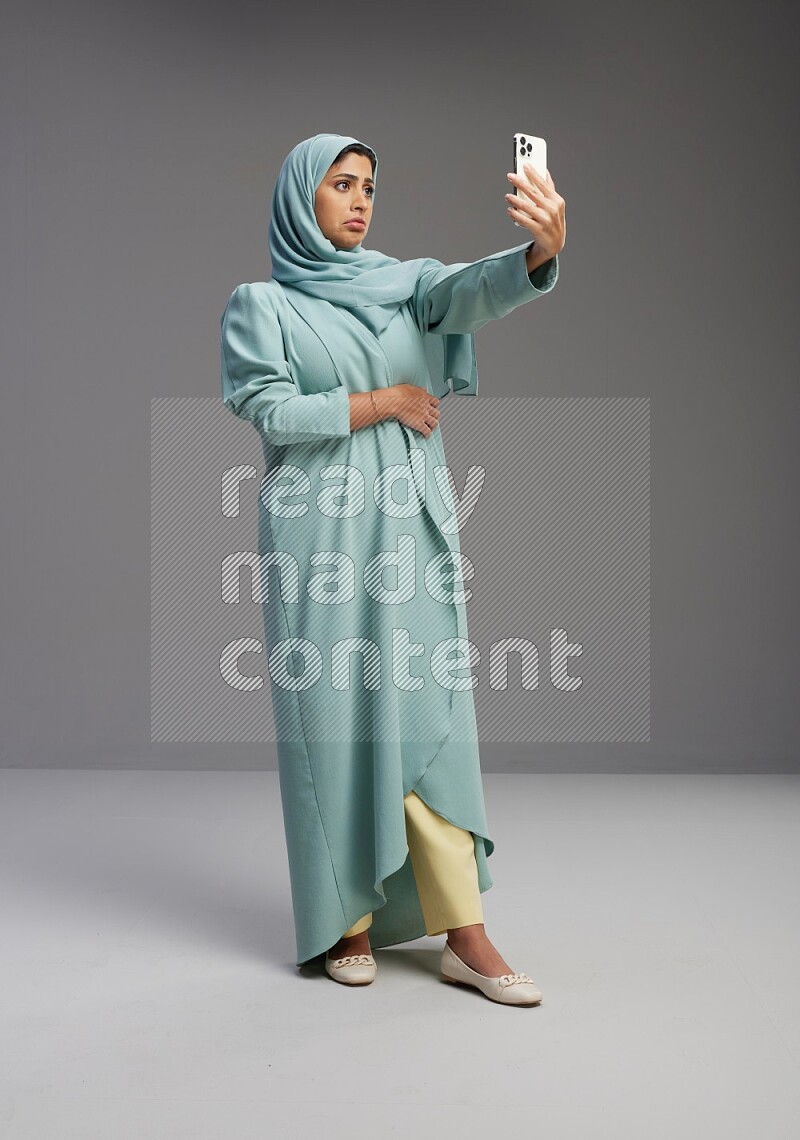 Saudi Woman wearing Abaya standing taking selfie on Gray background