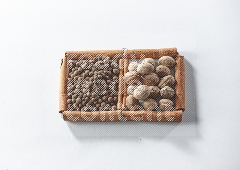 مربعان من أعواد القرفة ممتلئان ببهار الفلفل الحلو وجوزة الطيب علي خلفية بيضاء