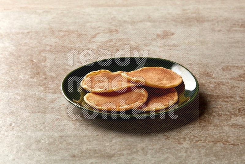 Four stacked plain mini pancakes in a green plate on beige background