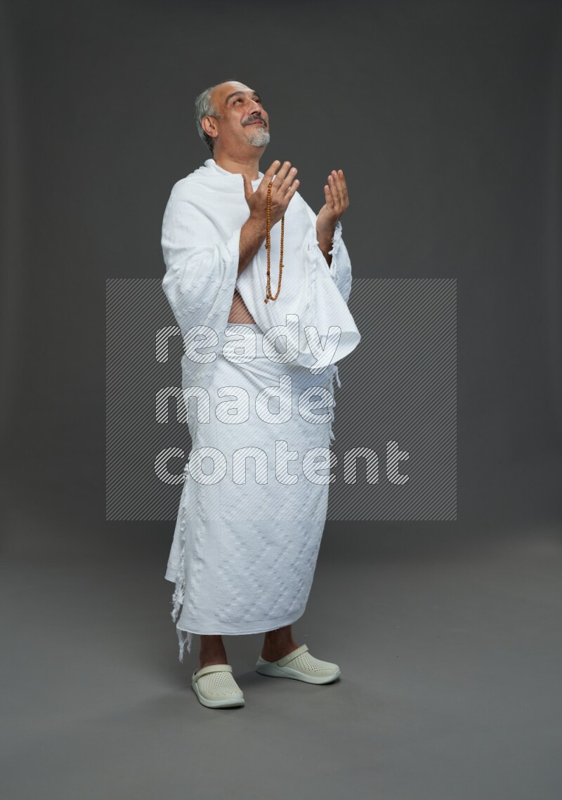 A man wearing Ehram Standing dua'a on gray background