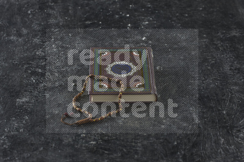 Quran with a prayer beads on textured black background