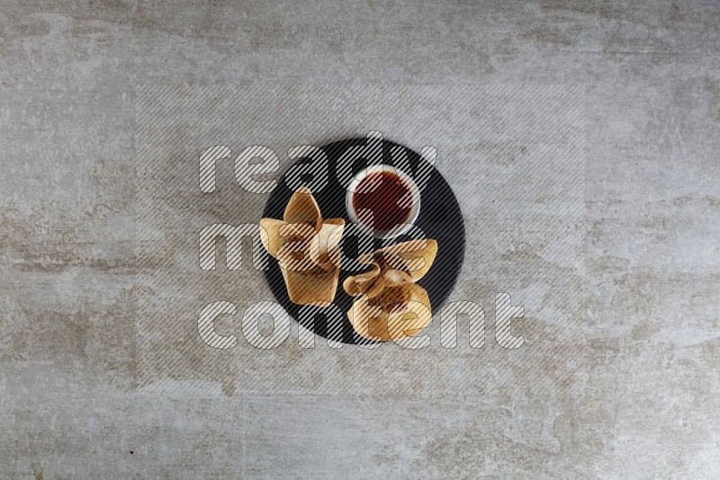 wonton cups with soy sauce ramkin on circle slate on grey textured counter top