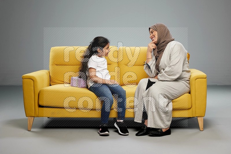 A girl sitting hiding a gift behind her back for her mother on gray background