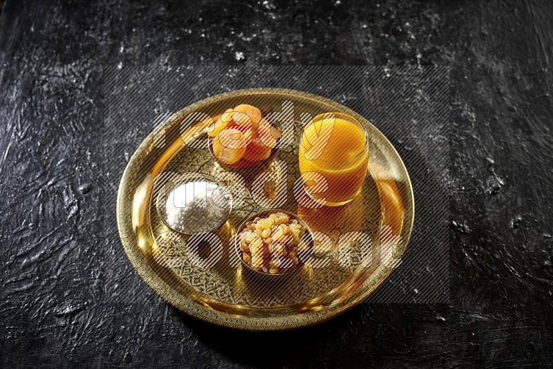 Dried fruits in metal bowls with qamar eldin on a tray in dark setup