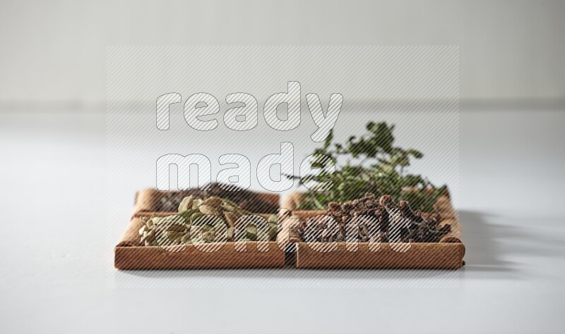 4 مربعات من أعواد القرفة ممتلئة بالشاي والهيل والنعناع والقرنفل على أرضية بيضاء