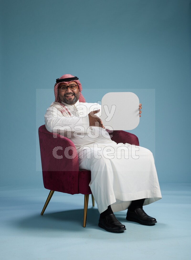 Saudi Man with shimag sitting on chair holding social media sign on blue background