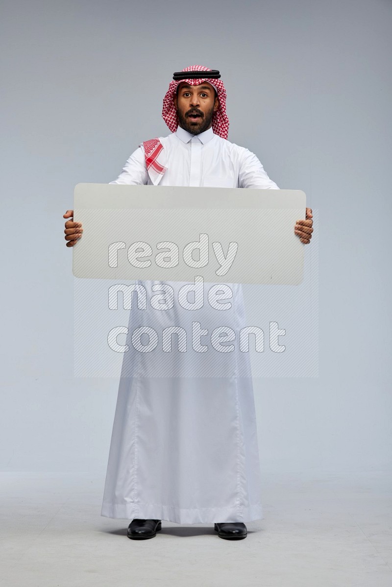 Saudi man Wearing Thob and shomag standing holding board on Gray background