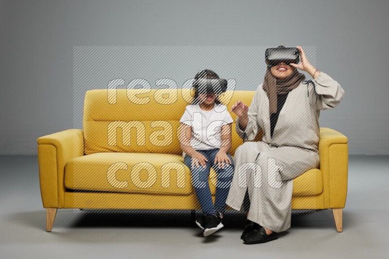 A girl and her mother sitting playing with VR on gray background