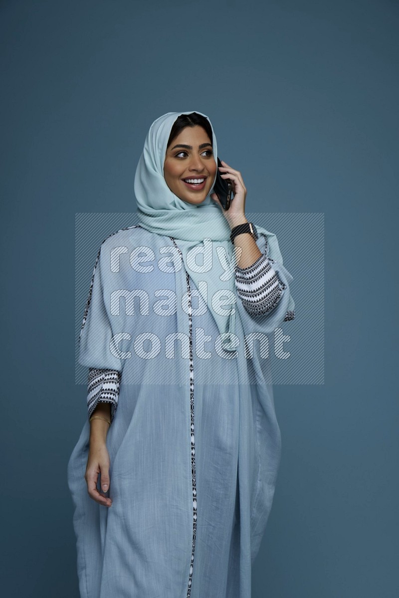A Saudi woman having a Call in a blue background wearing blue Abaya with hijab