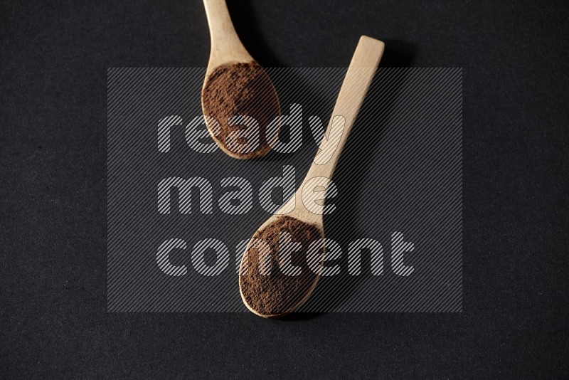2 wooden spoons full of cloves powder on a black flooring