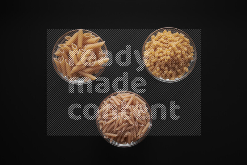 Different pasta types in glass bowls on black background